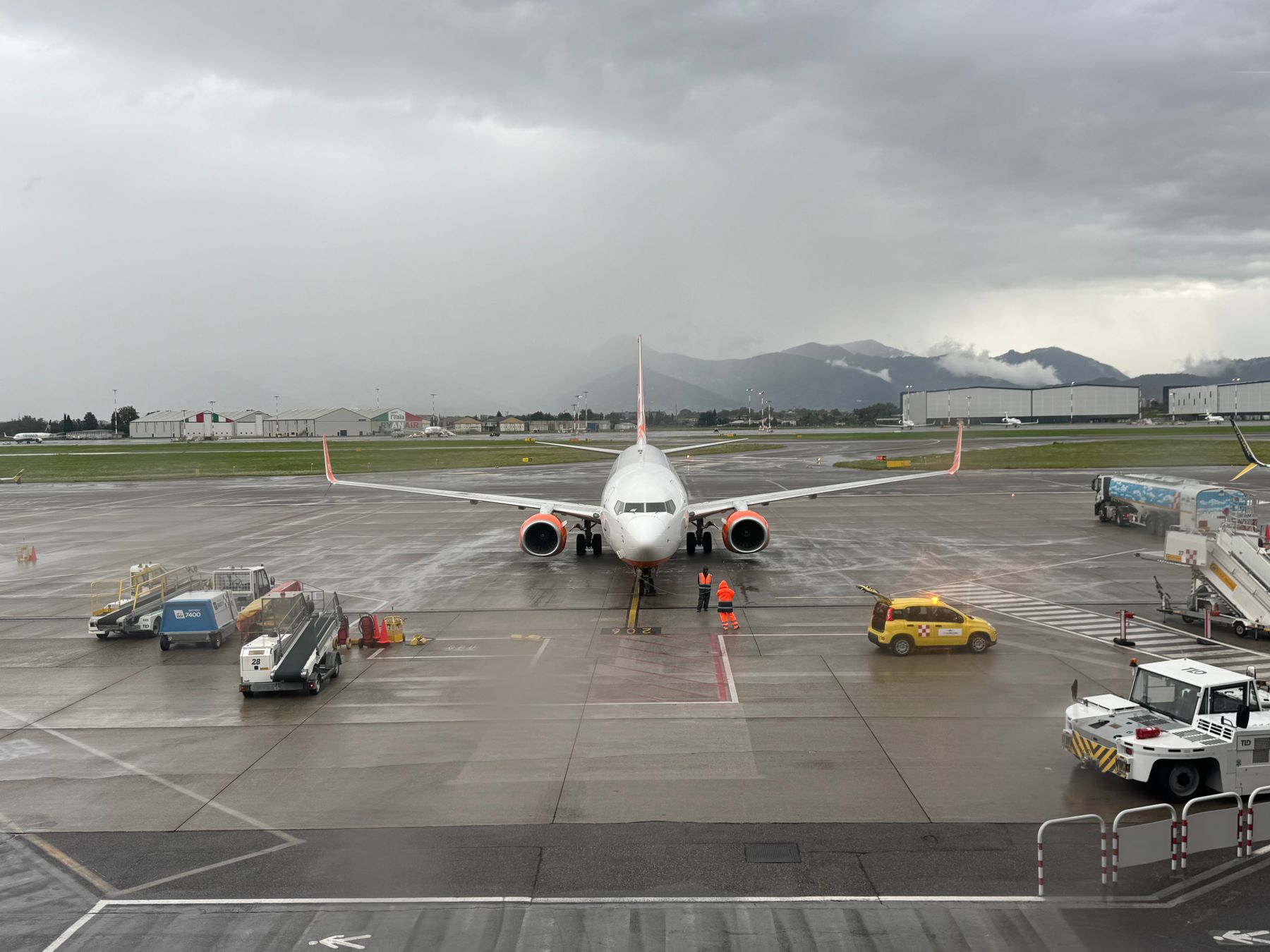 Airport ground workers and equipment on a rainy apron.